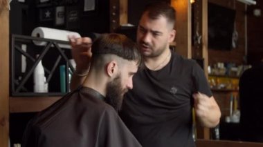 Berber erkek müşterinin saçını kesiyor.