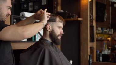 Berber erkek müşterinin saçını kesiyor.