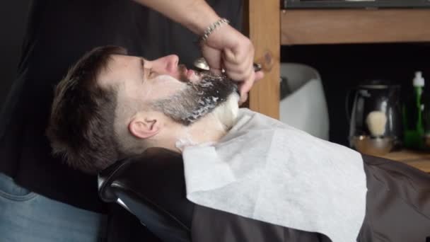 Парикмахер наносит пену для бритья на бороду клиента — стоковое видео