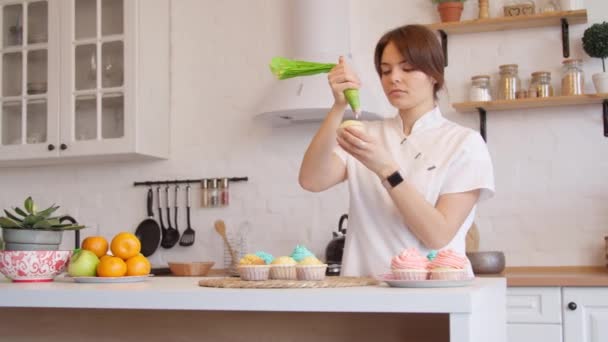 Vrouw glazuur cupcakes in de keuken — Stockvideo