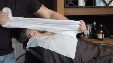 Berber müşterinin yüzünü havluyla örtüyor.