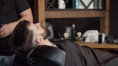 Berber müşterinin kafasına su püskürtüyor.