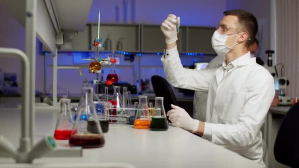 Молодий вчений змішуючи кольорові рідини — стокове відео