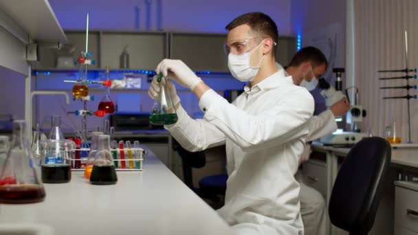 Jovem cientista misturando líquidos coloridos — Vídeo de Stock