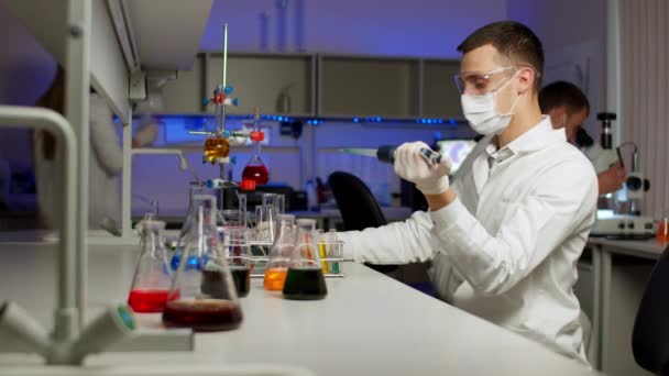 Jonge wetenschapper mengen gekleurde vloeistoffen — Stockvideo