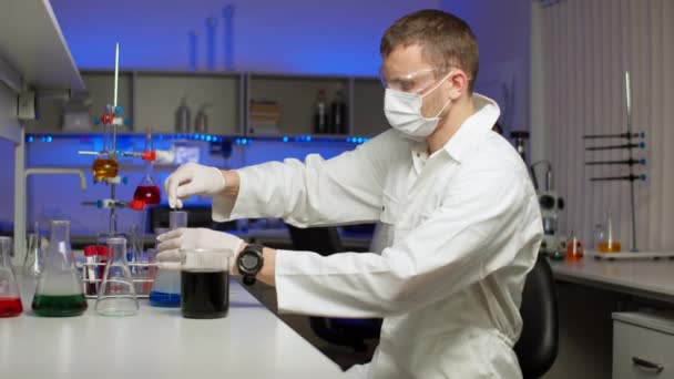 Jonge wetenschapper mengen gekleurde vloeistof — Stockvideo