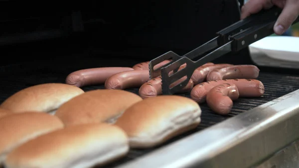 Kolbászt grillezett hot doghoz forgató személy — Stock Fotó