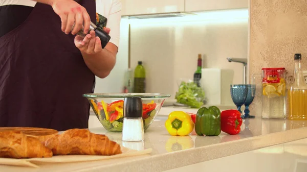 Man seasoning fresh green salad with salt