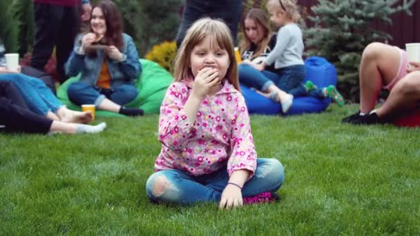 Liten flicka äter en varmkorv i trädgården — Stockvideo