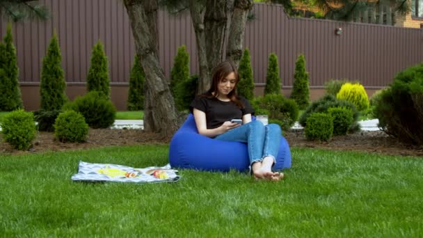 Młoda kobieta za pomocą smartfona w ogrodzie — Wideo stockowe