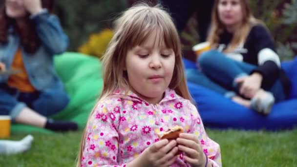 Niña comiendo un perrito caliente en el patio trasero — Vídeo de stock