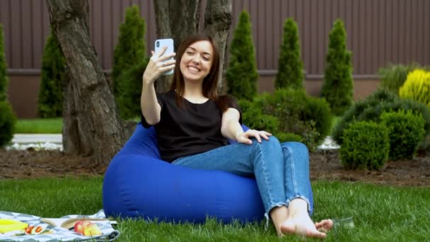 Молодая женщина проводит видеозвонок в саду — стоковое видео