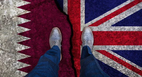 Uomo d'affari si erge sulla bandiera incrinata del Regno Unito e Qatar. Concetto politico — Foto Stock