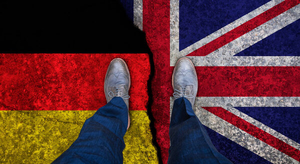 Деловой человек стоит на потрескавшемся флаге Великобритании и Германии. Политическое понятие
