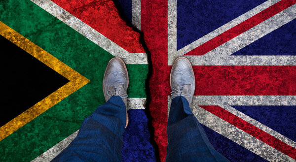Деловой человек стоит на потрескавшемся флаге Великобритании и Южной Африки. Политическое понятие
