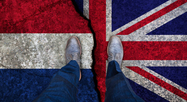 Деловой человек стоит на потрескавшемся флаге Великобритании и Нидерландов. Политическое понятие
