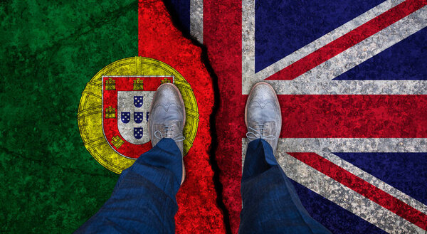 Деловой человек стоит на потрескавшемся флаге Великобритании и Португалии. Политическое понятие
