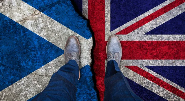 Uomo d'affari si erge sulla bandiera incrinata del Regno Unito e della Scozia. Concetto politico — Foto Stock