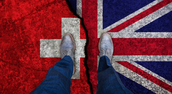 Uomo d'affari si erge sulla bandiera incrinata del Regno Unito e della Svizzera. Concetto politico — Foto Stock