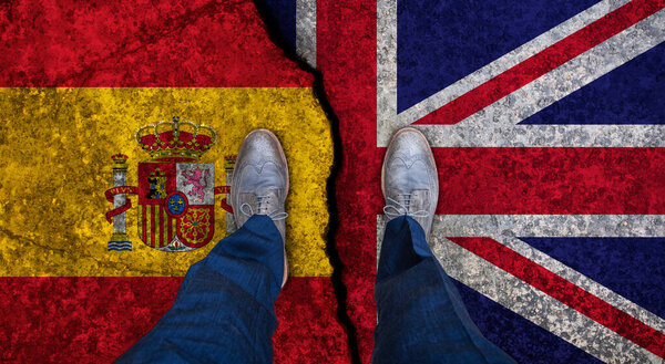 Деловой человек стоит на потрескавшемся флаге Великобритании и Испании. Политическое понятие

