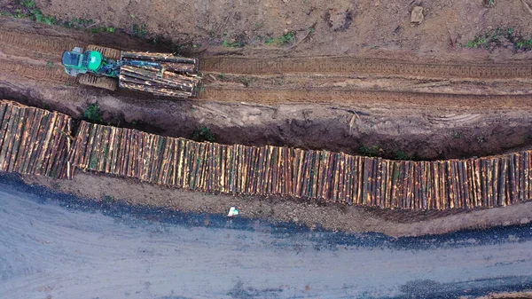Vista aérea de la madera transportada a lo largo de una pista fangosa por maquinaria pesada . —  Fotos de Stock