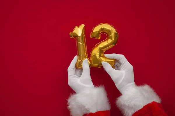 12 days of christmas. Santa hands holding 12th day balloon on red background — Stock Photo, Image