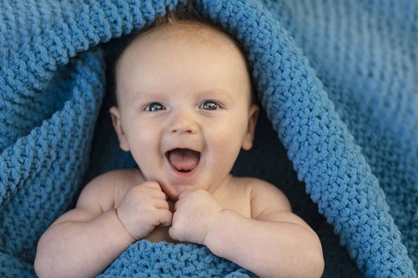 Een vrolijke lachende baby gewikkeld in een knusse bllue deken — Stockfoto
