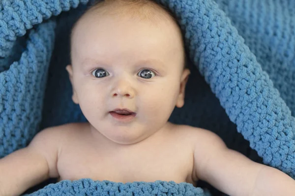 Um menino bonito envolto em um cobertor azul acolhedor olhando para a câmera — Fotografia de Stock