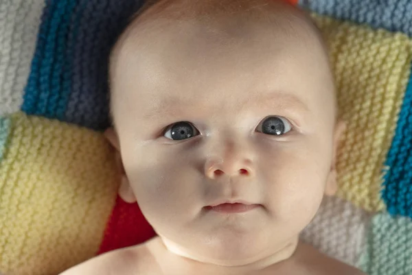 Portrait of a cute baby with blue eyes laying on a knitted balnket — Stock Photo, Image