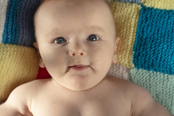 Portrait of a cute baby with blue eyes laying on a knitted balnket — Stock Photo, Image