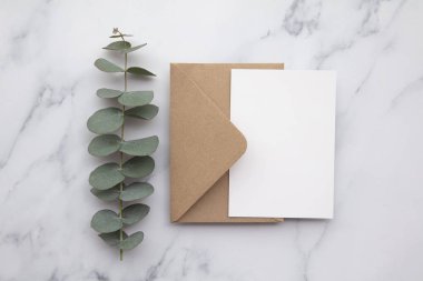 Boş beyaz kart ve okaliptüs yapraklı zarf. Boş davet.
