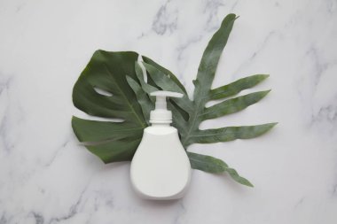 Blank white cosmetic products on a marble background with tropical palm leaf