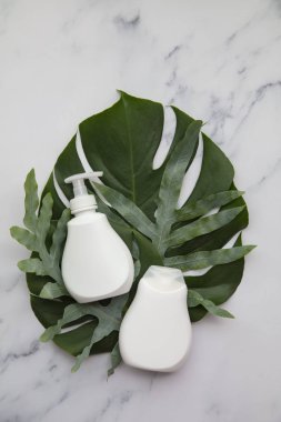 Blank white cosmetic products on a marble background with tropical palm leaf