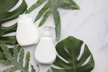 Blank white cosmetic products on a marble background with tropical palm leaf