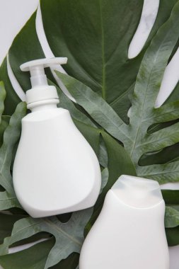 Blank white cosmetic products on a marble background with tropical palm leaf