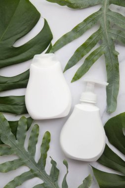 Blank white cosmetic products on a marble background with tropical palm leaf