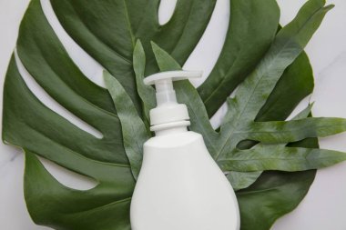 Blank white cosmetic products on a marble background with tropical palm leaf