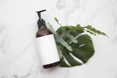 Cosmetic product bottle with blank label on a tropical leaf