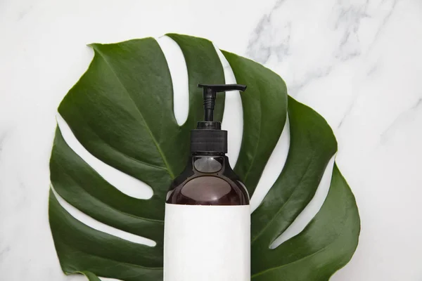 Botella de producto cosmético con etiqueta en blanco en una hoja tropical — Foto de Stock