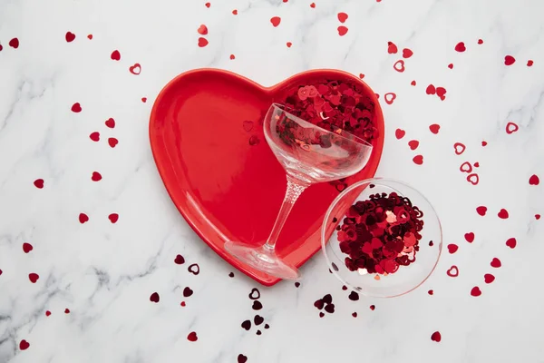 Valentines dinner background. Red heart plate with champagne glass and confetti — Stockfoto