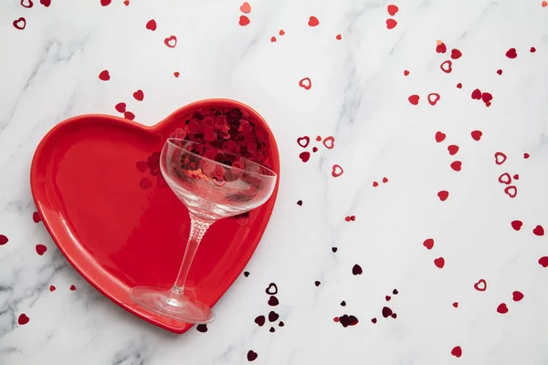 Valentines dinner background. Red heart plate with champagne glass and confetti — Stockfoto