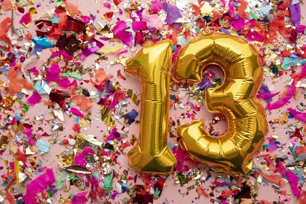 Number 13 gold birthday celebration balloon on a confetti glitter background