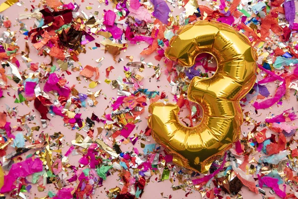 Number 3 gold birthday celebration balloon on a confetti glitter background