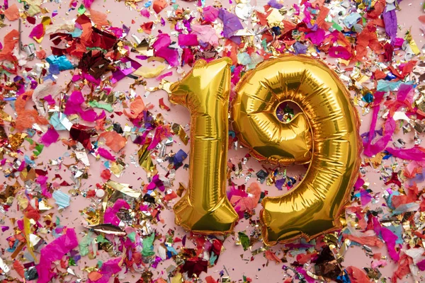 Number 19 gold birthday celebration balloon on a confetti glitter background