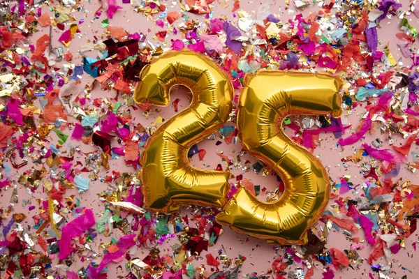 Number 25 gold birthday celebration balloon on a confetti glitter background — Stok fotoğraf