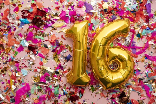 Number 16 gold birthday celebration balloon on a confetti glitter background — Stok fotoğraf