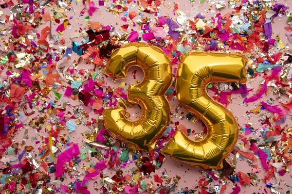 Number 35 gold birthday celebration balloon on a confetti glitter background