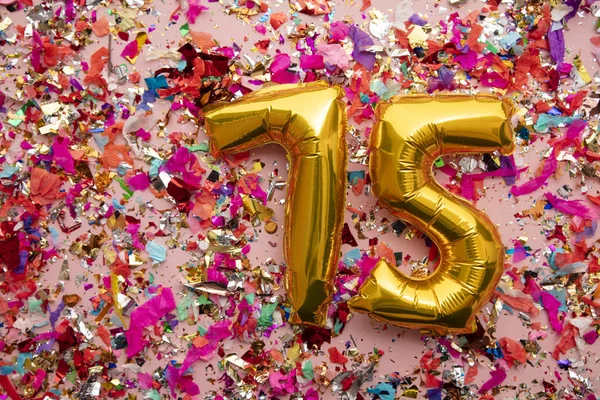 Number 75 gold birthday celebration balloon on a confetti glitter background