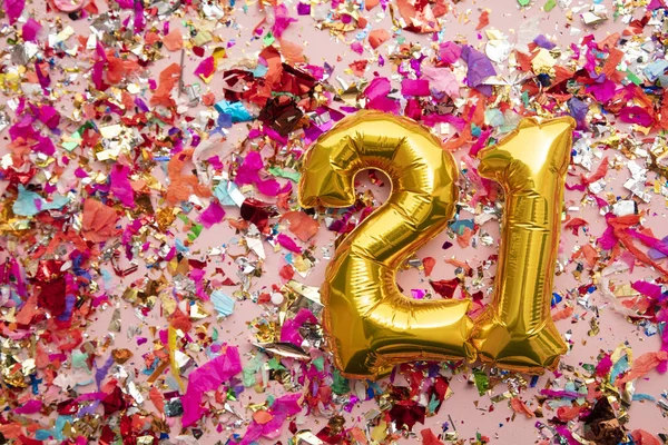 Number 21 gold birthday celebration balloon on a confetti glitter background