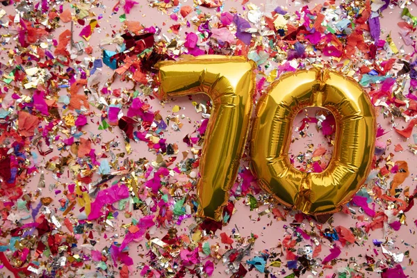 Number 70 gold birthday celebration balloon on a confetti glitter background